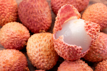 Chinese fruits and oriental foods concept with picture of one lychee fruit peeling the bumpy skin to expose the juicy delicate pulp on top of many lychees with copy space