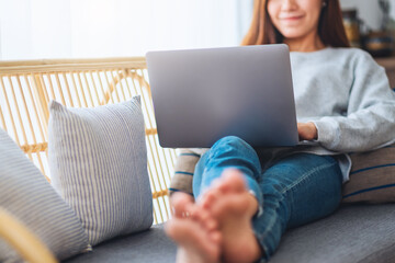 A beautiful woman using and working on laptop computer while lying on a sofa at home