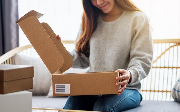 A beautiful young asian woman receiving and opening a postal parcel box at home for delivery and online shopping concept