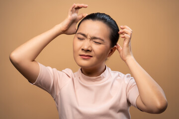 Asian woman scratching her head standing isolated on beige background.