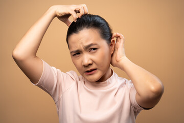 Asian woman scratching her head standing isolated on beige background.