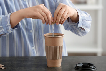 Woman with adding sugar to coffee in cup on table