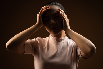 Asian woman was sick with headache standing isolated on beige background. Low key.