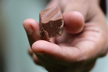 Woman's hand offering unwrapped dark chocolate, close-up.