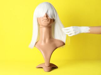 Female hand and mannequin with wig on color background
