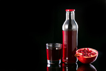 Pomegranate juice in a glass, bottle and half of pomegranate on a black background with copy space. Vitamins, healthing food and drink.