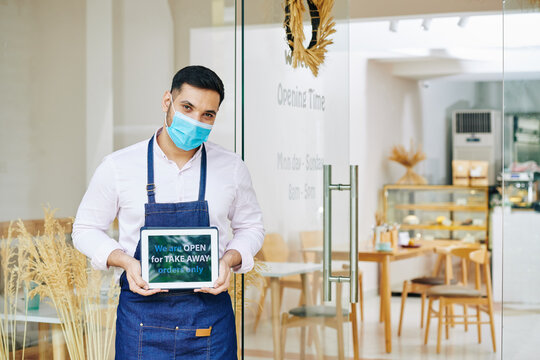 Portrait Of Young Bakery Shop Owner Holding Tablet Computer Informing Customers That The Cafe Is Open For Take Away Orders Only