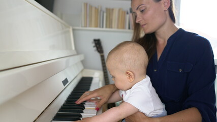 A cute mommy playing a white piano with her baby boy