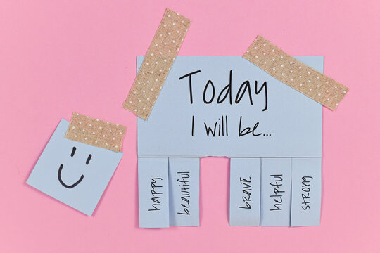 Motivational concept with blue tear-off stub note with text 'Today I will be...' and words 'happy, beautiful, brave, helpful' and 'strong' on pink background