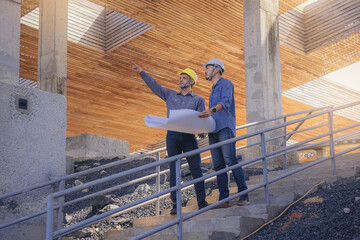 Structural engineer and architect working with blueprints discuss at the stairway, outdoors building construction site.