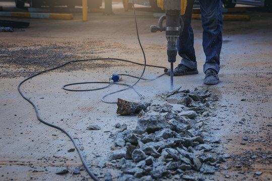 Worker drilling cement concrete with jackhammer machine at outdoor construction site