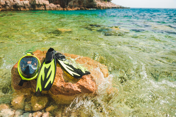 Plakat snorkeling mask with flippers at rock in sea water