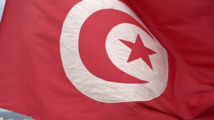 Closeup view of red Tunisian flag standing on roof of high building isolated at aerial view cityscape background.