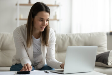 Millennial woman using computer e-bank application calculates incomes feels satisfied. Housewife manage family budget pay domestic utility bills, bookkeeper do work remote job make financial analysis