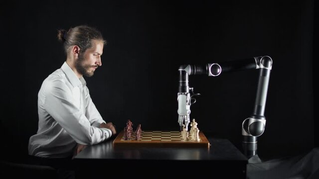 Modern technology, man playing chess with a robot, the confrontation between man and artificial intelligence, futuristic robotic arm participates in the game.