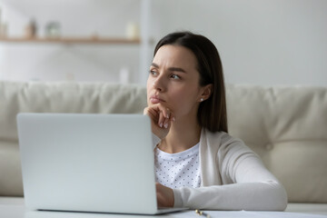 Pensive student girl sit in front of laptop thinking over task do assignment distracted form study....