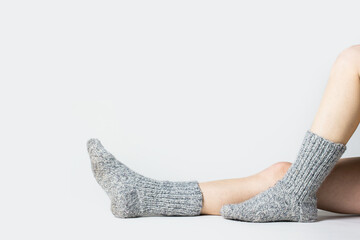 Woman sits on the floor in warm gray socks on a light background. Only legs visible