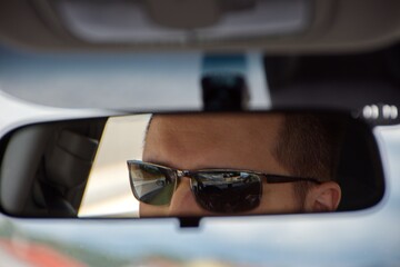 The face of a young man driving as seen in the rear view mirror