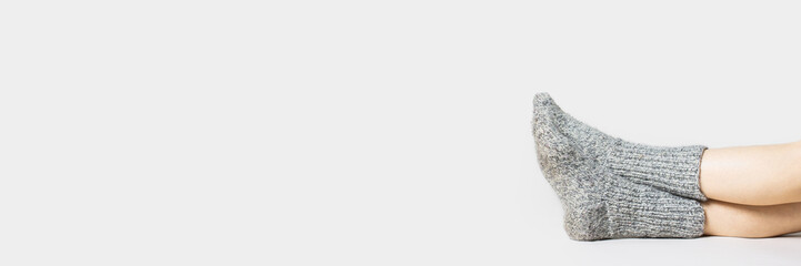 Woman sits on the floor in warm gray socks on a light background. Only legs visible