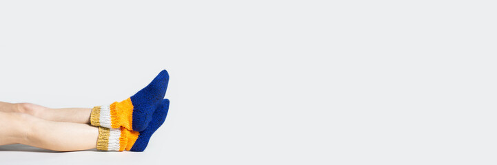 Woman sits on the floor in warm multi-colored socks on a light background. Only legs visible