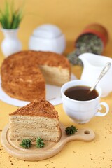 tasty homemade honey cake on yellow background with a cup of coffee, milk and flowers