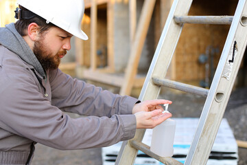 Builder wearing hardhat and disinfecting hands by disinfectant.