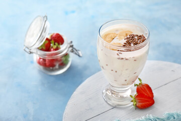 Glass of yogurt with banana and flax seeds on color background