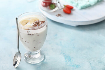 Glass of yogurt with banana and flax seeds on color background