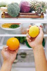 Man choosing citrus fruit for refreshing drink, he is taking orange and lemon out of fridge