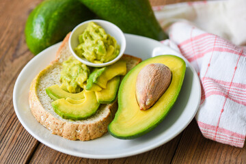 Avocado sliced half and avocado dip mashed on white plate background fruits healthy food concept - avocado toast