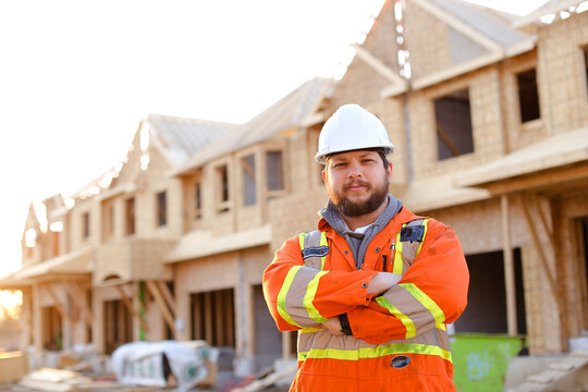 Male foreman standing on construction site with building in background.