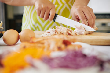 Housewife cutting bacon in thin slices when cooking breakfast at home