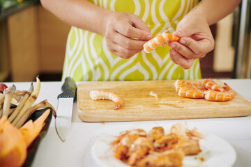 Close-up image of housewife peeling boiled shrimps when cooking dinner at kitchen table