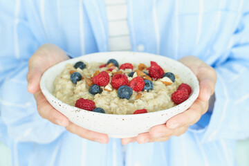Faceless woman holds in hands breakfast, oatmeal porridge with berries and nuts