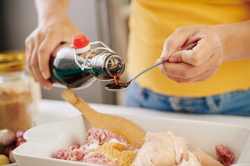 Hands of person adding spoon of soy sauce into bowl with ground meat