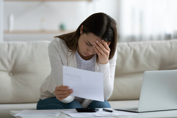 Stressed woman sit on sofa read bad news notification paper letter from bank about debt or...