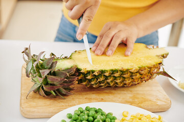 Close-up image of woman cutting fresh ripe pineaaple with sharp ceramic knife