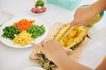 Hands of cook making bowl out of pineapple to fill it with vegetables and brown rice