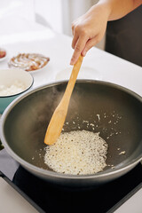 Woman frying diced onion in cooking pan and mixing it with wooden spatula