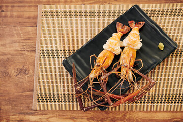 Cooked spiny lobsters served on black plate with piece of garlic paste