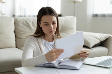 Woman sit at coffee table at home holding paper read personal touching letter from friend or relative looking like she missed or upset by sad news, frustrated female received postal message concept