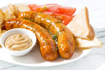 fried pork sausages with potatoes and mustard on plate, closeup