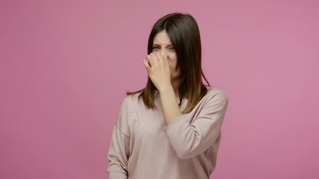 Repulsion to bad smell. Brunette girl grabbing nose with fingers, holding breath to avoid stink, awful fart gases, intolerable odor, showing stop gesture. studio shot isolated on pink background