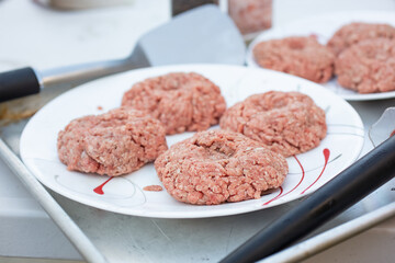 A view of several raw burger patties on a plate, ready for grilling.