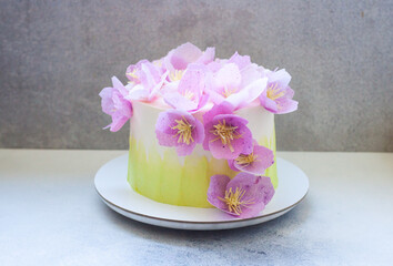 Tender green birthday cake with purple and pink paper flowers on grey background.
