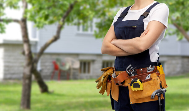 repair, construction and building concept - woman or builder with working tools on belt over living house yard with garden background