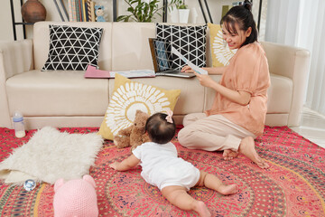 Happy smiling young businesswoman with financial document in hands looking at her crawling little baby