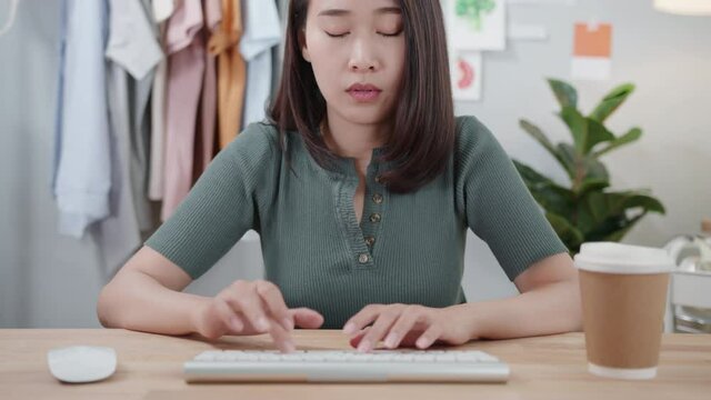 POV Shot Of Young Asian Female Freelancer Sitting At Desk Using Desktop Computer And Looking At Screen While Typing On Keyboard Doing A Report, Surfing Internet At Home Office. Remote Working Concept