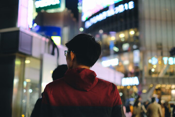 Young man walking in front of department store in big city at night