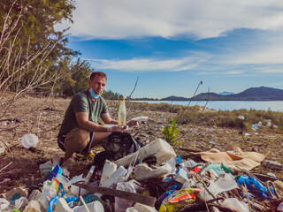 Man in gloves pick up plastic that pollute sea and forest. Problem of spilled rubbish trash garbage...